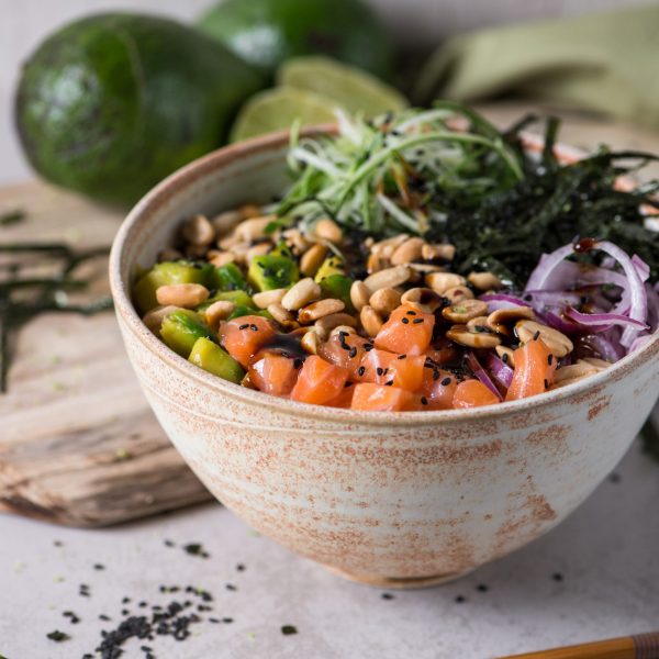 Poke, a Hawaiian dish consisting of japanese rice in a bowl topped with a variety of fresh ingredients such as raw fish, avocado, onions, peanuts, cucumber, seaweed, sesame seeds and lemon zest.